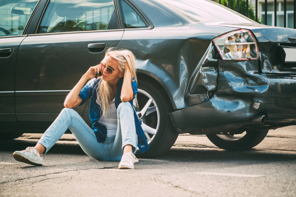woman on phone next to car accident calling attorney